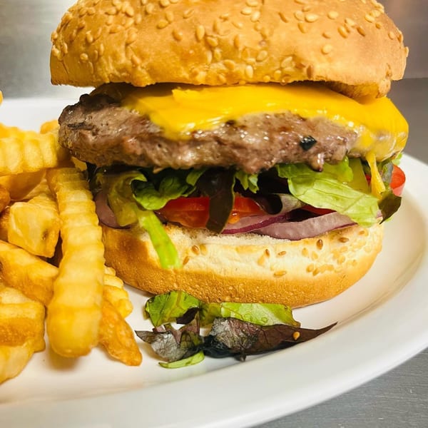 A juicy cheeseburger with lettuce, tomato, and onion, served with crinkle-cut fries on a white plate.