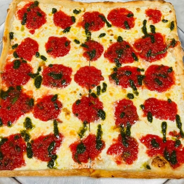 A rectangular Soprano's Pizza with melted mozzarella, dollops of red sauce, and pesto drizzle.