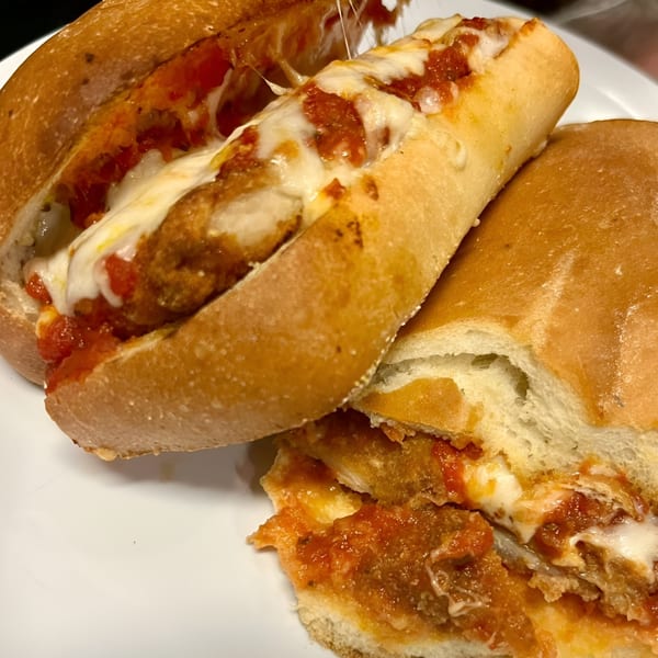 Two Soprano's Pizza meatball subs with melted cheese and marinara sauce on a white plate.