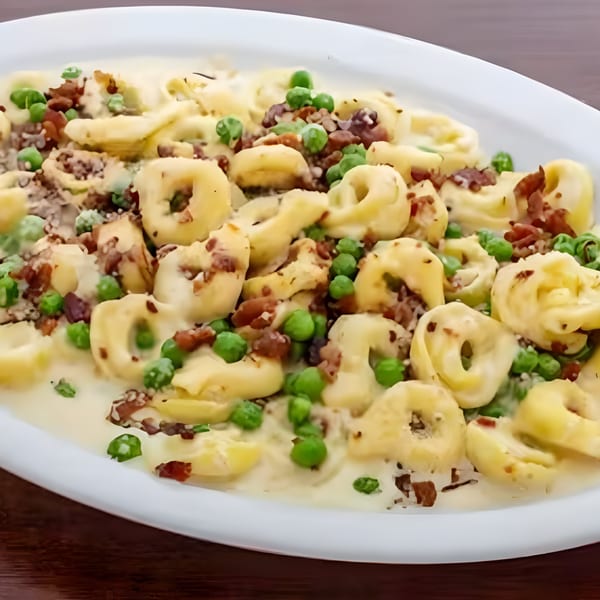 Tortellini pasta in a creamy sauce with peas and bacon bits on a white plate.