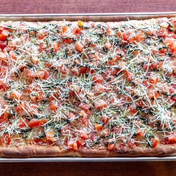 Soprano's Pizza's rectangular pizza with diced tomatoes, shredded cheese, and pesto drizzle.